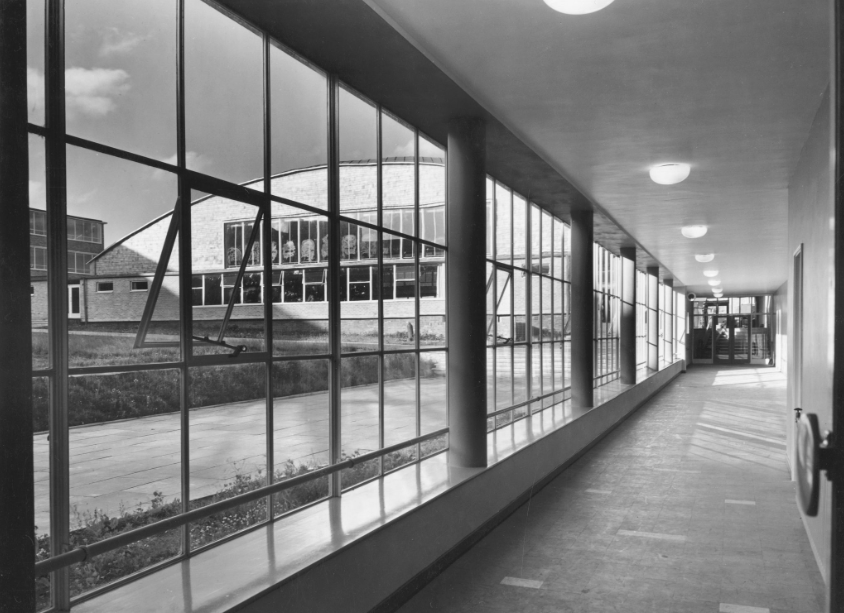 A black and white photo of The Halley Academy building taken through a window from a corridor.