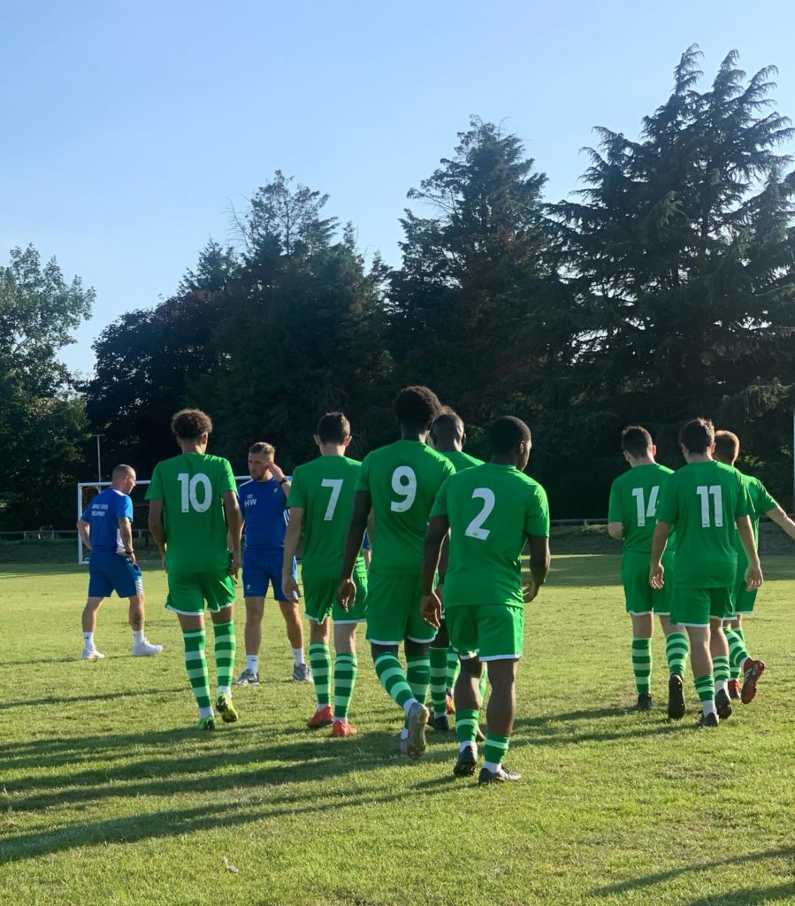 A group of male students are seen dressed in green-coloured Football kit, each with a number on their backs, walking together towards a pitch.