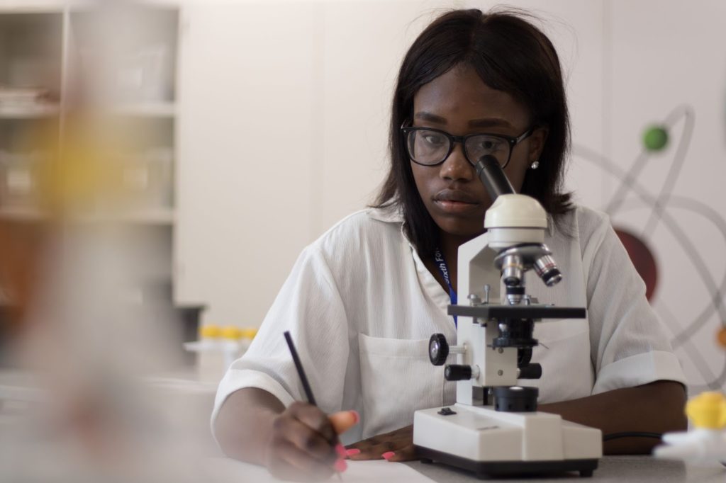A Halley Academy student is pictured looking down a microscope lens and holding a pencil in her hand.