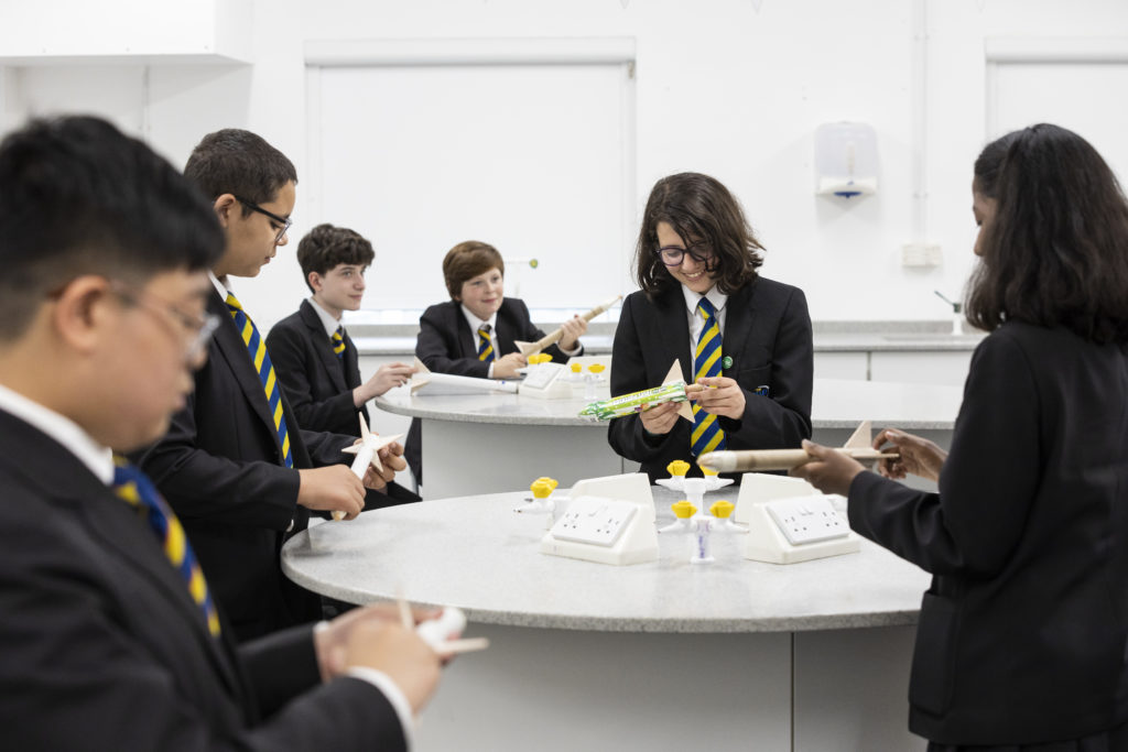 Some students are pictured conversing with each other in a Science lab, as they analyse the model rockets they have created using recycled materials.