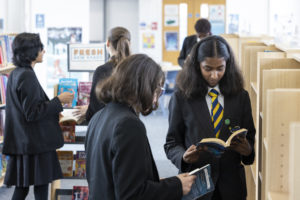 Some students can be seen in the School Library, reading books and talking with one another.