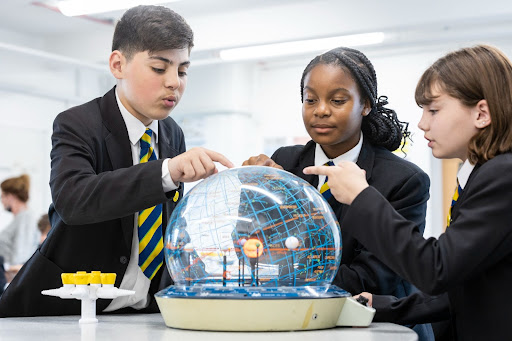 Three Year 7 students are pictured looking closely at a model of our solar system and pointing to it during a Science lab class.