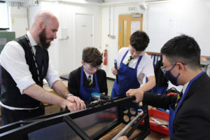 Three young students are pictured using drills and hammers under the supervision of a member of staff, during a Design & Technology class at The Halley Academy.
