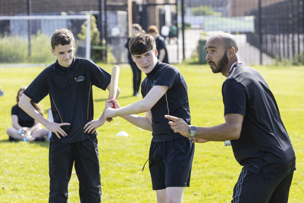 Two students are pictured wearing their PE Kit, being instructed by a teacher on the academy grounds.