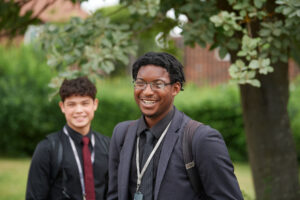 Two male Post-16 students are seen smiling together outdoors on a grass area of the academy grounds.